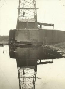 A derrick reflected in a "pool of oil" from the earliest Nebraska well.